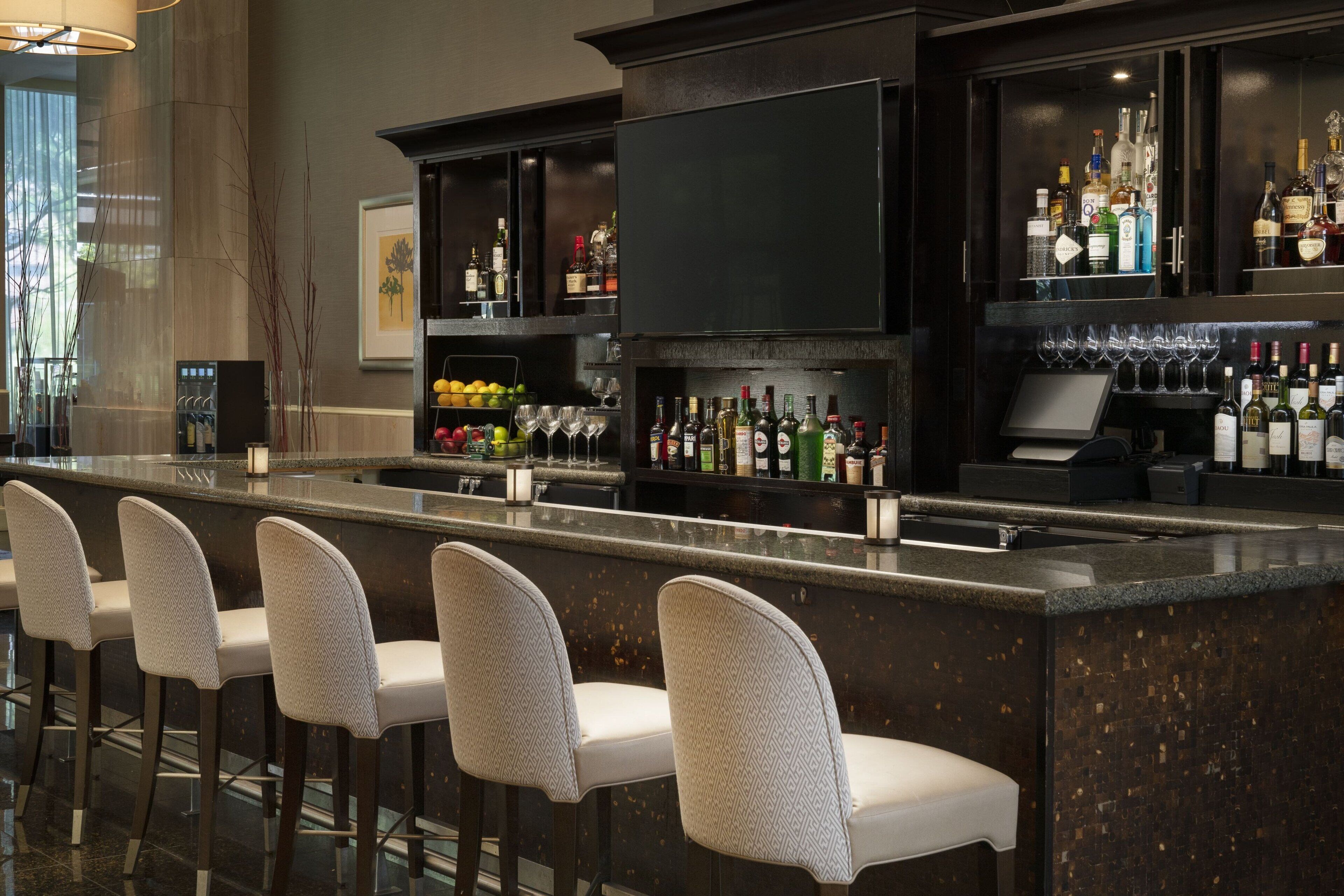 A bar area with a long counter, multiple stools, and a variety of bottles and glasses.