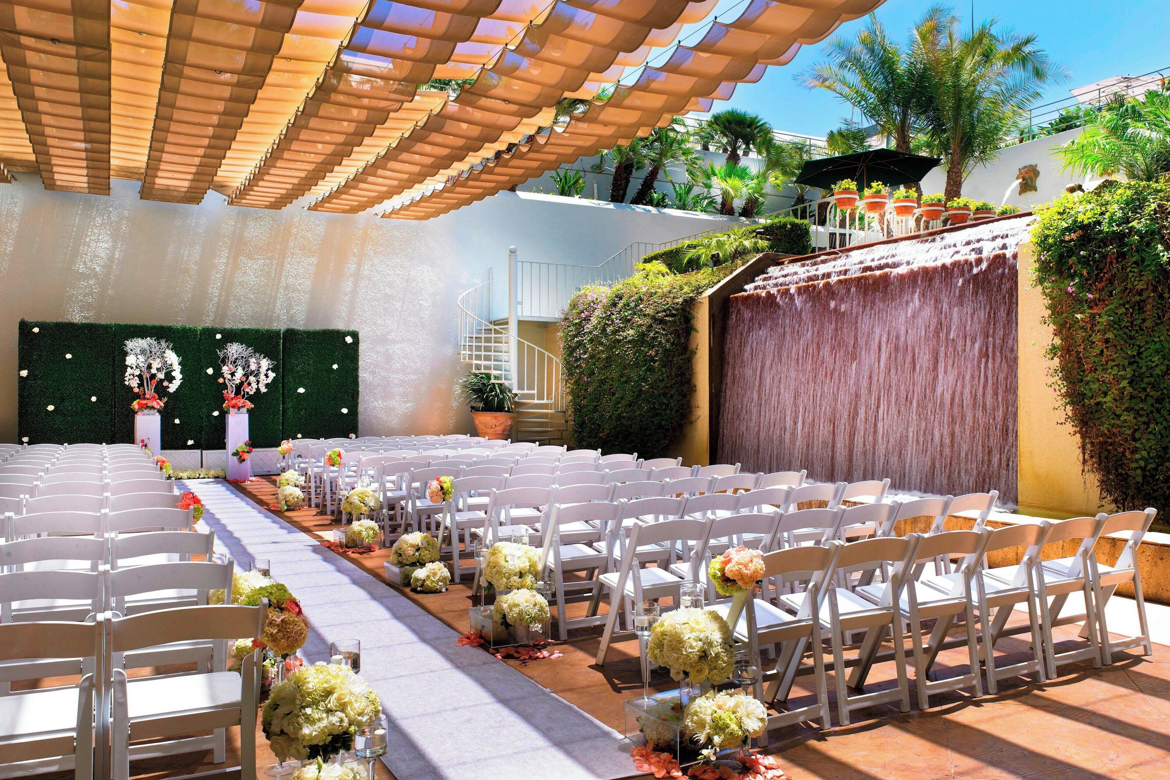 A wedding venue with rows of white chairs, floral centerpieces, and a covered walkway.