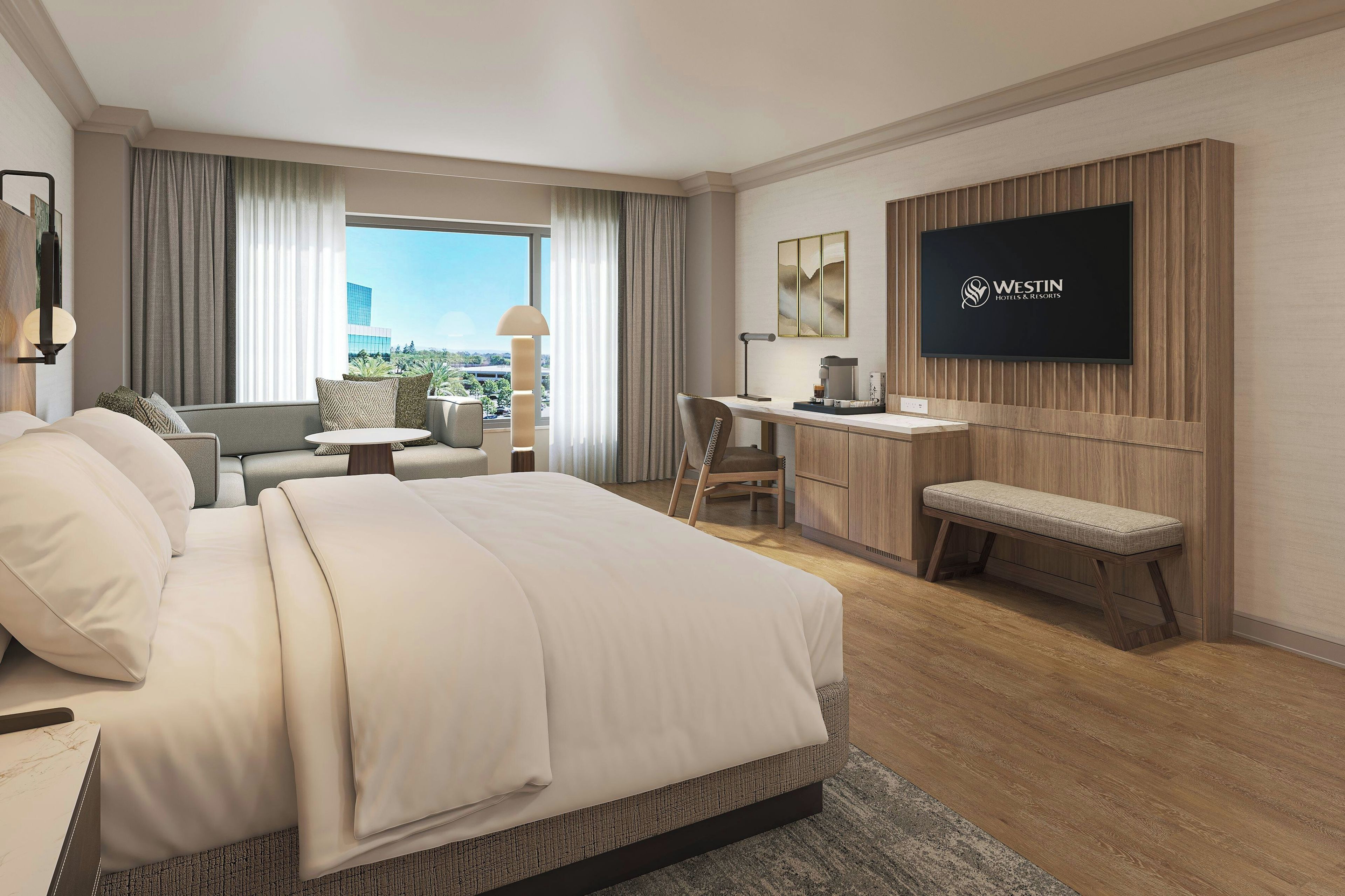 A hotel room with a bed, a desk, a chair, a TV, and a view of the city.