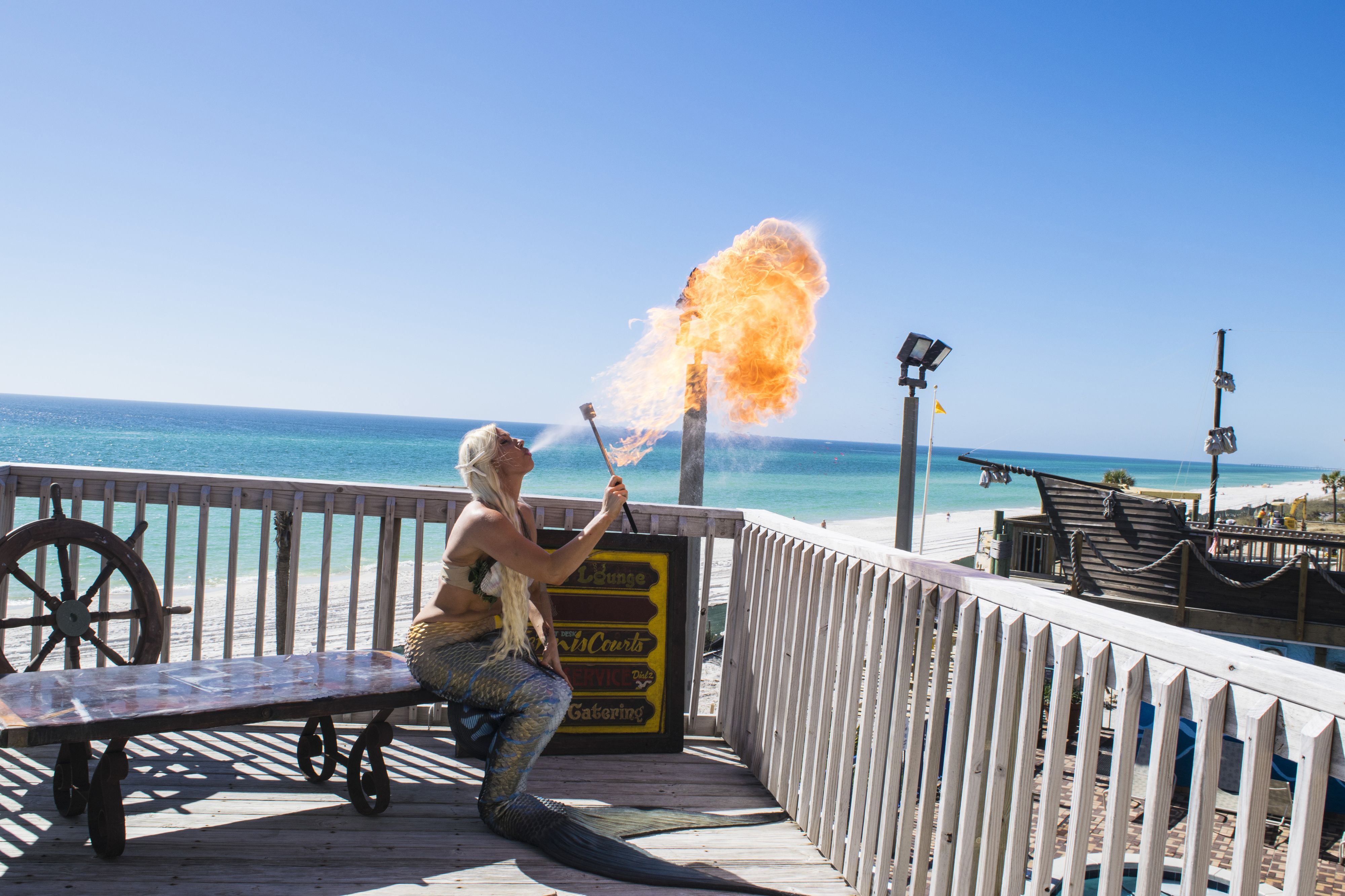 Eine Holzterrasse mit einem Schild, einer Sitzbank und Blick auf den Strand und das Meer.
