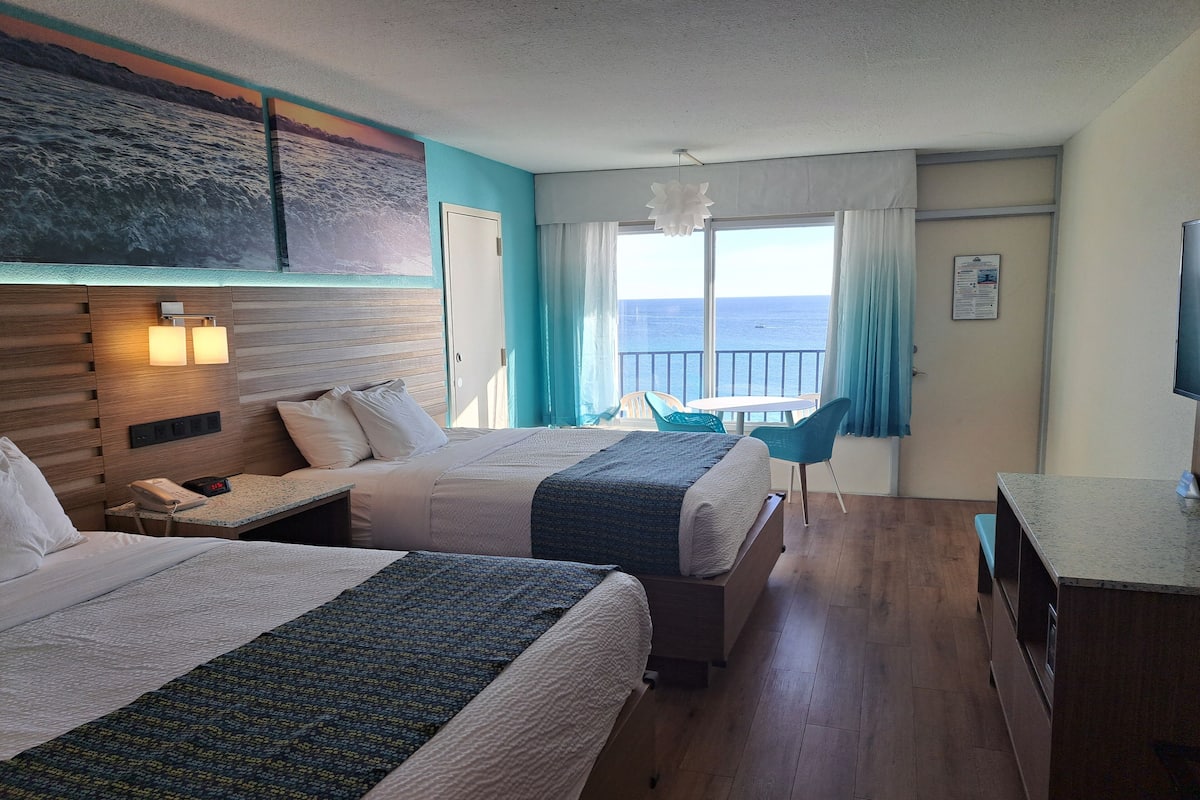 Habitación de hotel con dos camas, un escritorio, una silla y vista al mar.