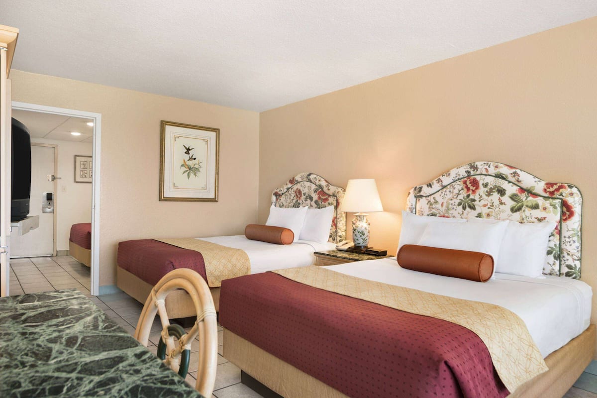 Habitación de hotel con dos camas, una zona de estar y una puerta que da a otra habitación.