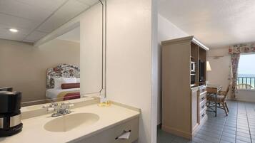 A hotel room with a large mirror, a double sink, a coffee maker, a TV, and a balcony with a chair.