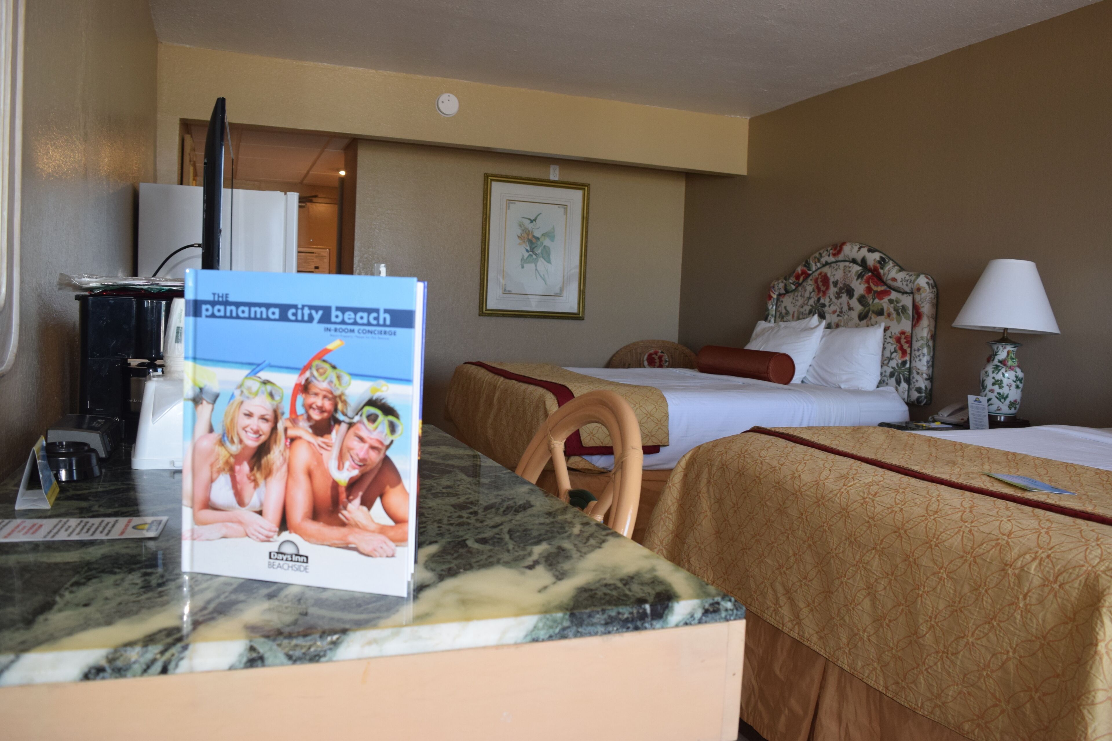 A hotel room with a bed, a desk, a chair, a lamp, and a framed picture on the wall.