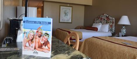A hotel room with a bed, a desk, a chair, a lamp, and a framed picture on the wall.