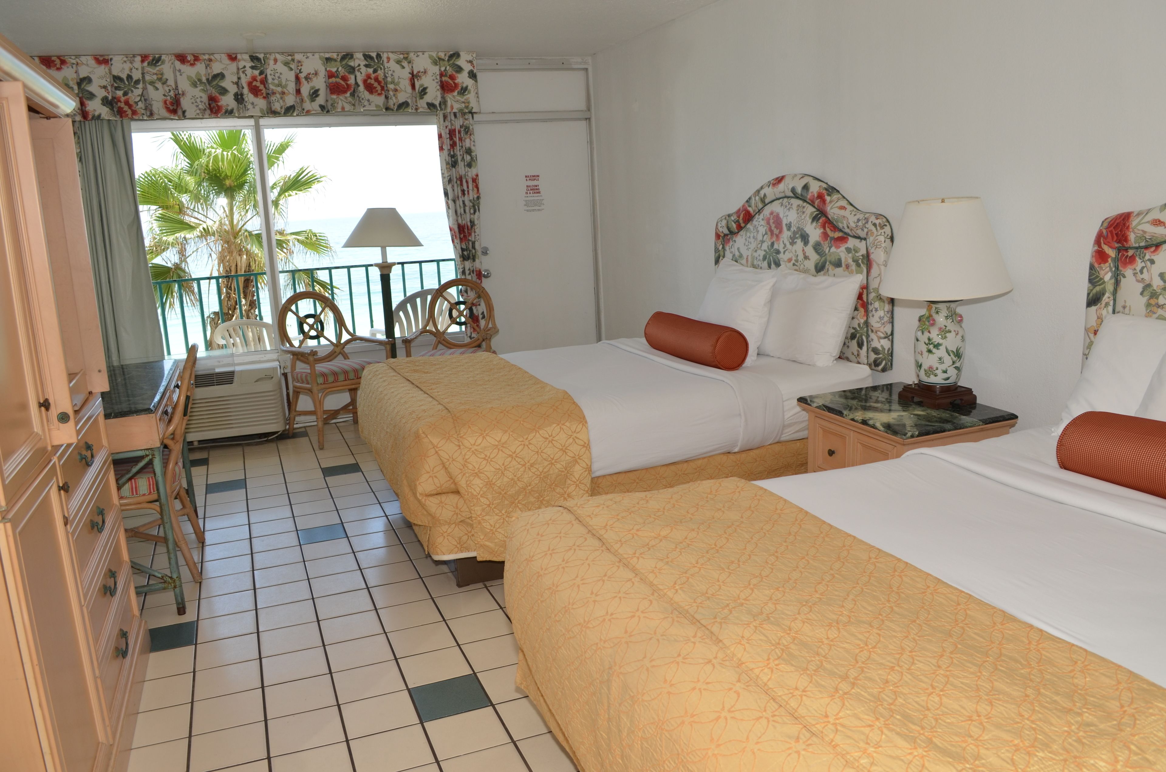 Een hotelkamer met twee bedden, een bureau, stoelen en uitzicht op palmbomen.