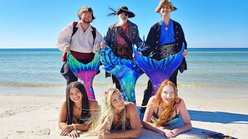 Un groupe de personnes se trouve sur une plage, avec un ciel dégagé et l’océan en arrière-plan.