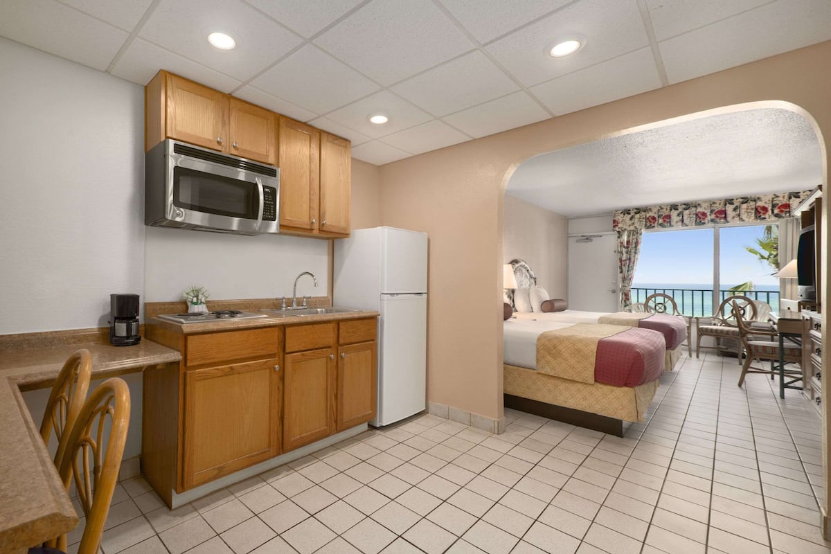 Una habitación de hotel compacta con kitchenette, una cama, un balcón con vistas y un área de comedor.