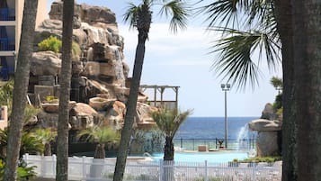 Área da piscina com vista para o oceano, cercada por palmeiras e formações rochosas.