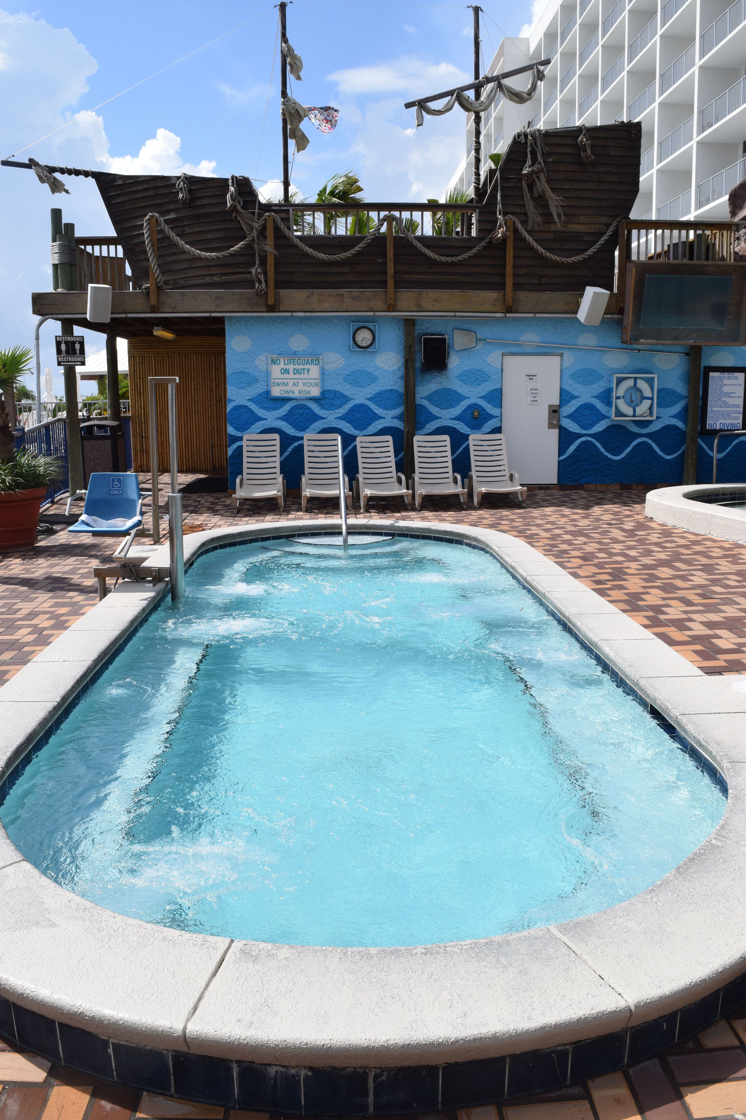 A swimming pool with a lifeguard station, lounge chairs, and a building with a nautical theme.