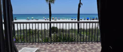 A beach view from a balcony with a tiled floor, palm trees, and beach umbrellas.