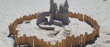 A sandcastle with two towers and a bridge on a sandy beach.