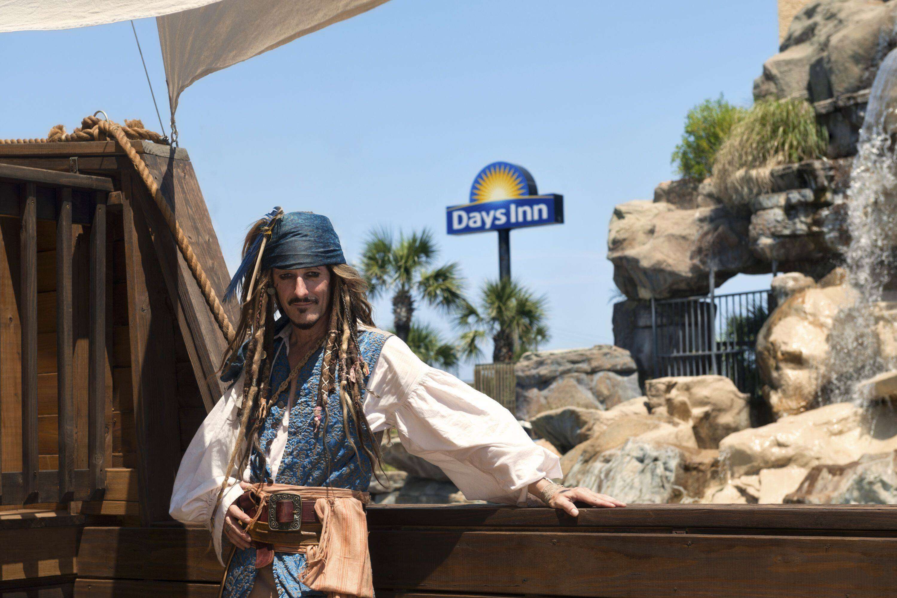 A person in a pirate costume leaning on a wooden structure with a Days Inn sign in the background.