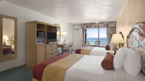 Une chambre d’hôtel avec deux lits, un bureau avec une télévision, une commode et une vue sur la mer.