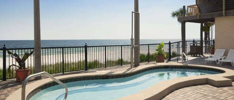 A swimming pool with a view of the beach, surrounded by a fence and potted plants.