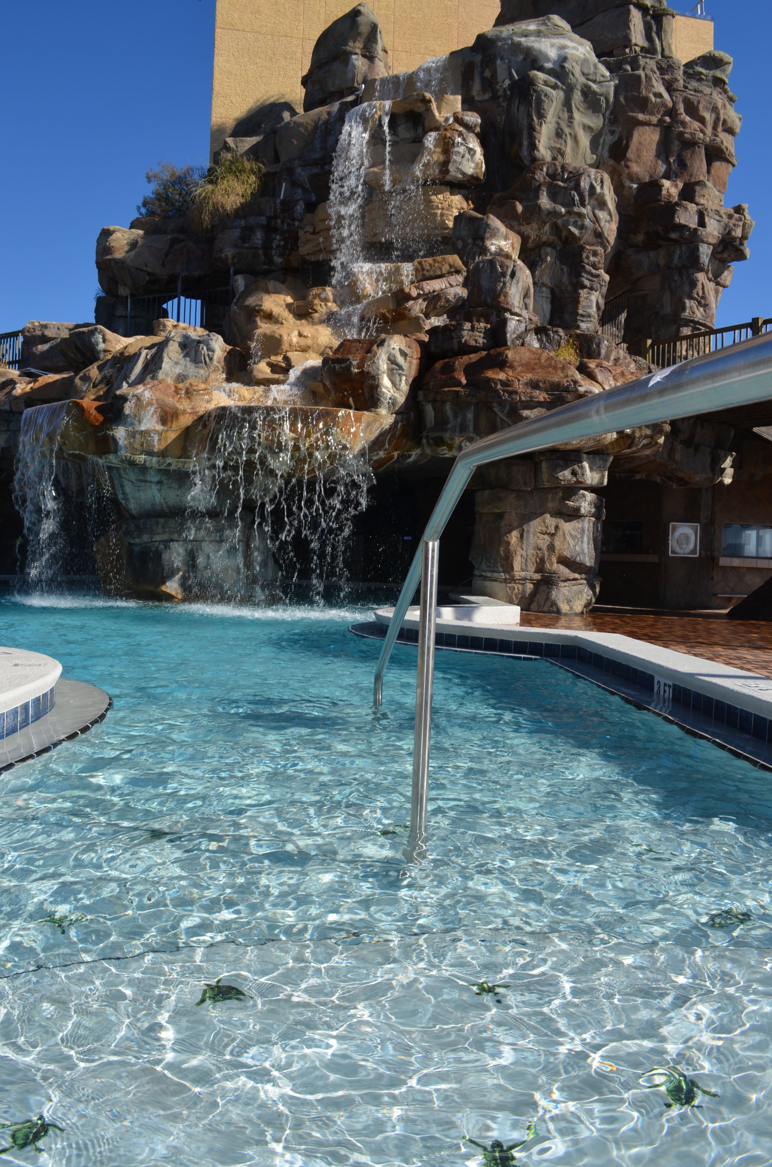 Una piscina cristalina con una cascada y un telón de fondo rocoso.