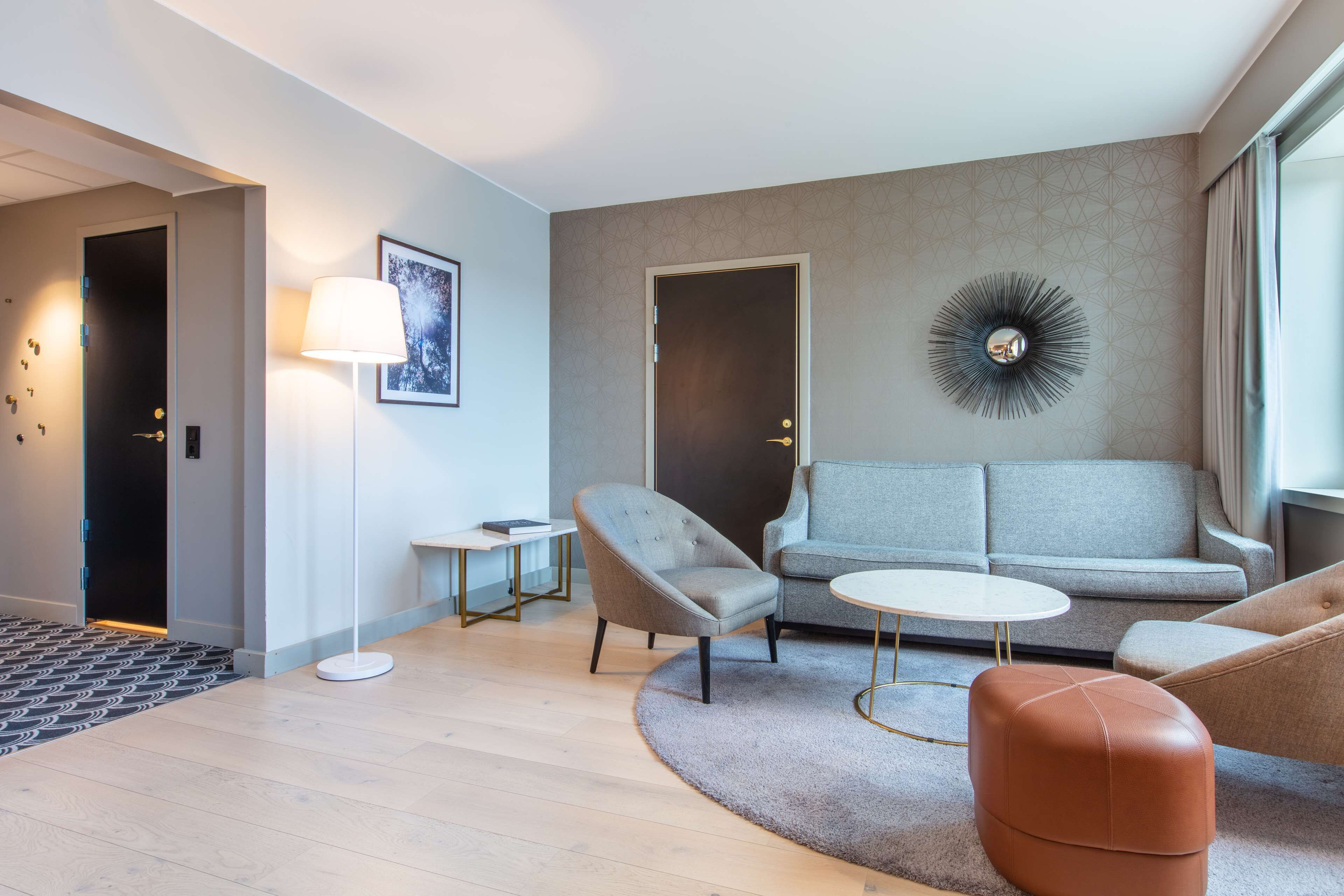 A modern living room with a grey sofa, a round coffee table, and a brown ottoman.