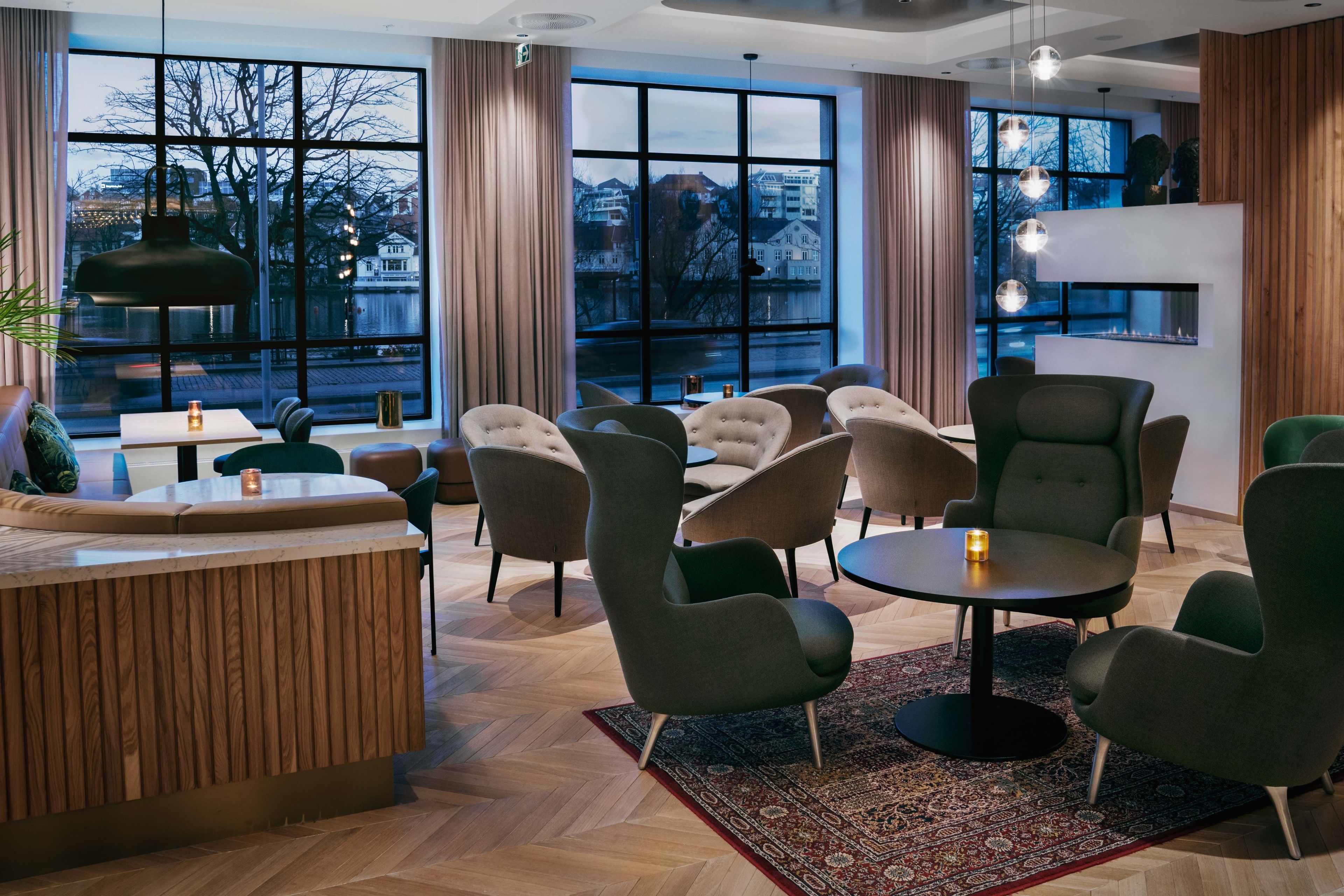 A modern lounge area with a wooden reception desk, multiple seating options, and large windows offering a view of the cityscape.