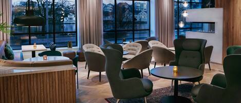 Uma área de lounge moderna com balcão de recepção de madeira, diversas opções de assento e grandes janelas com vista para a paisagem urbana.