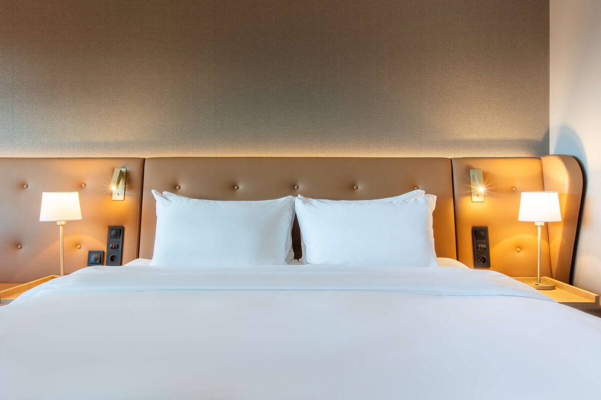 Hotellihuone, jossa on suuri sänky, kaksi yöpöytää ja sängynpääty, jossa on sisäänrakennettu valaistus.