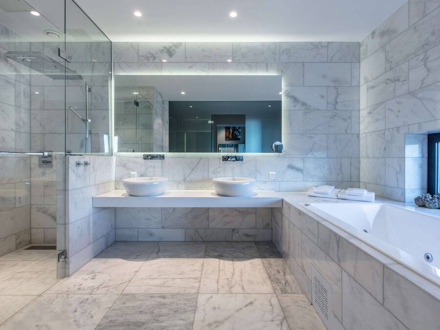 A modern bathroom with a glass-enclosed shower, a large mirror, two sinks, and a bathtub.