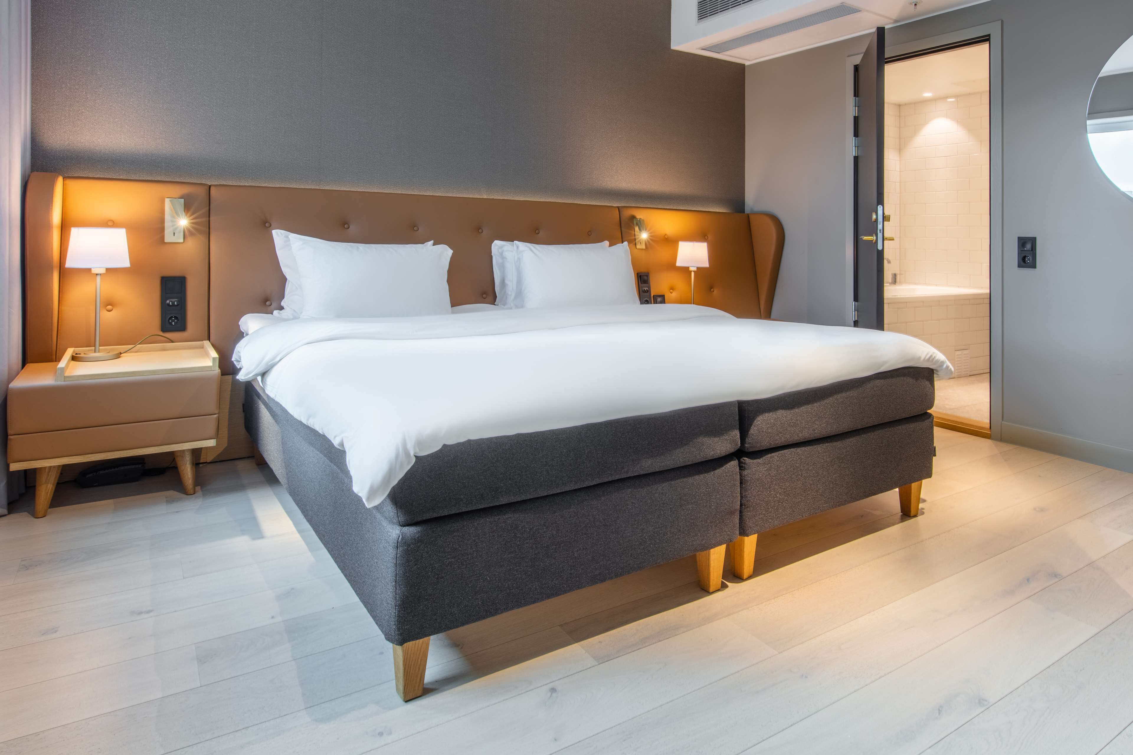 Una habitación de hotel moderna con una cama grande, mesitas de noche con lámparas y vistas al baño.