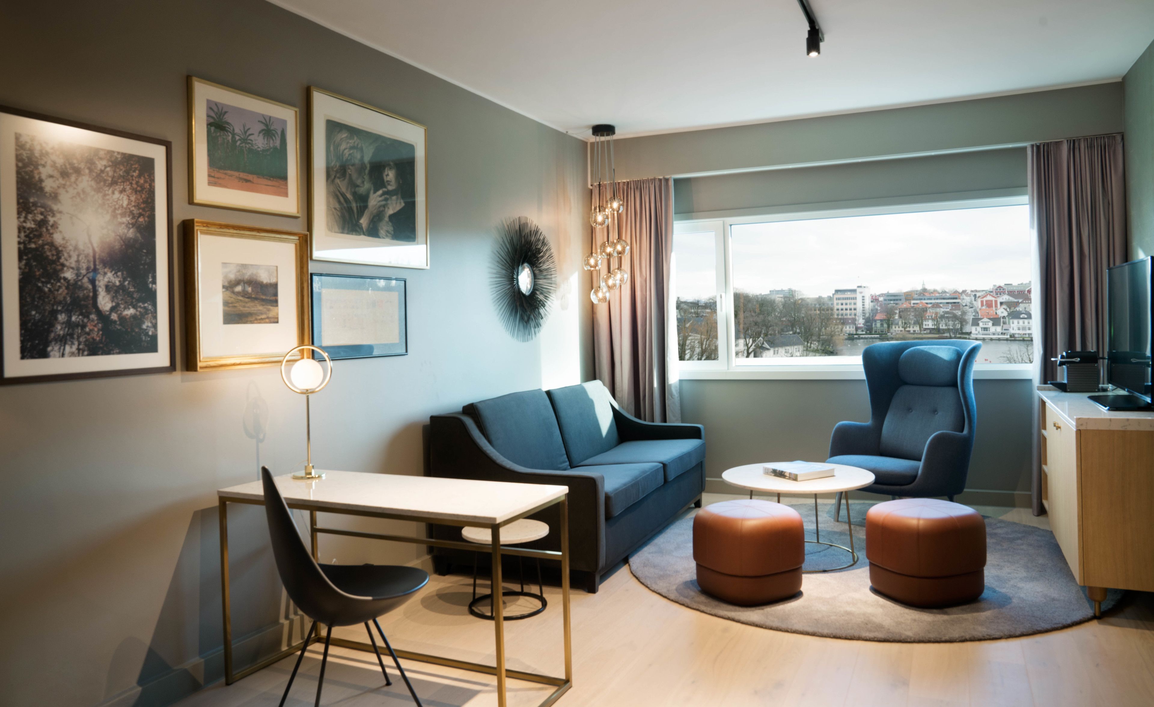 A modern living room with a sofa, armchair, and ottoman, a dining table with chairs, and a TV.
