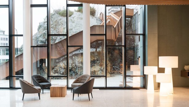 Un hall espacioso con ventanas amplias, sillas modernas y techo de madera.