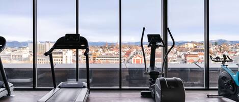 A gym with exercise equipment and large windows offering a city view.