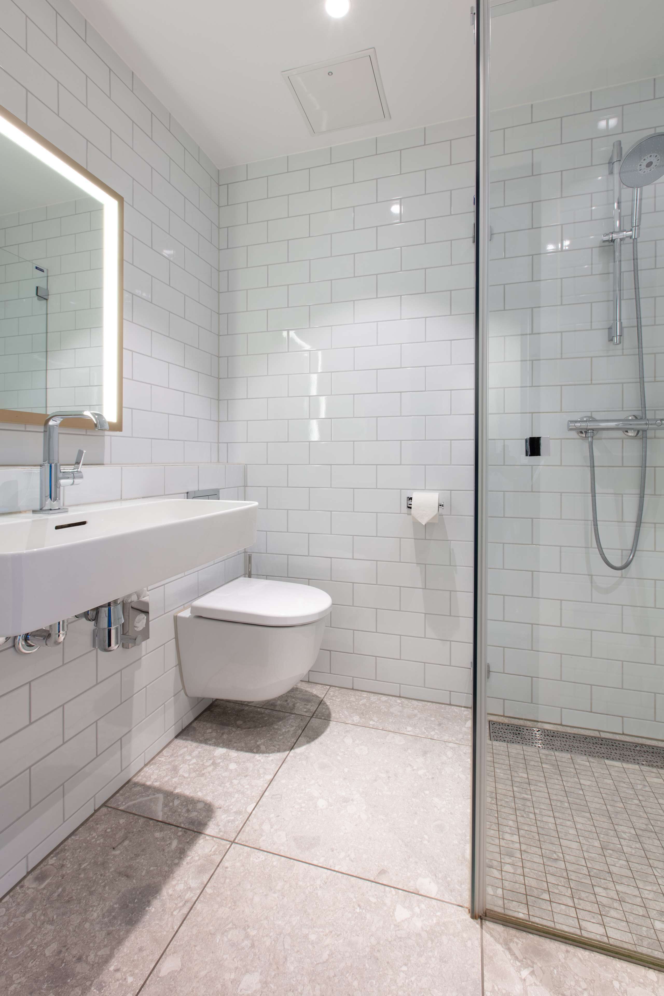 A modern bathroom with white subway tiles, a glass shower enclosure, a white sink, and a toilet.