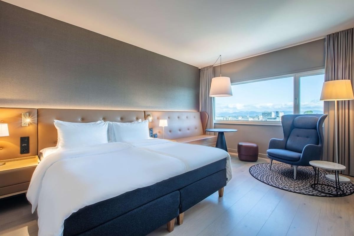 A hotel room with a large bed, a desk, a chair, and a view of the city.