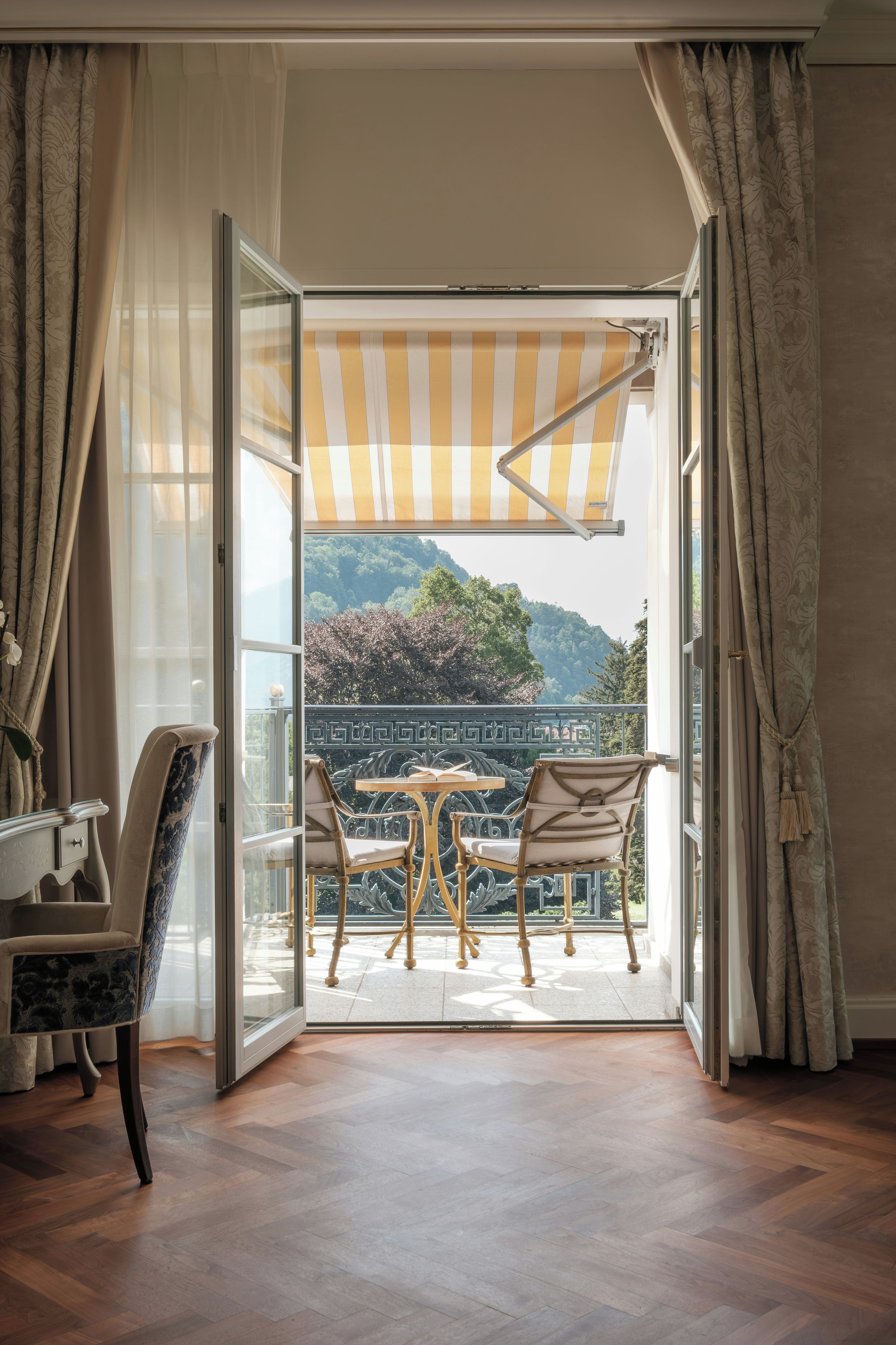 An open room with a view of a balcony, a table, two chairs, and a patterned curtain.