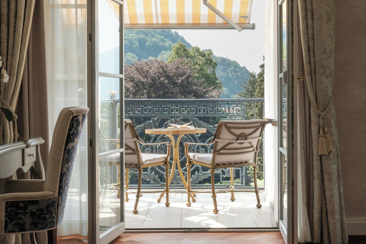 Habitación abierta con vista a un balcón, una mesa, dos sillas y una cortina estampada.