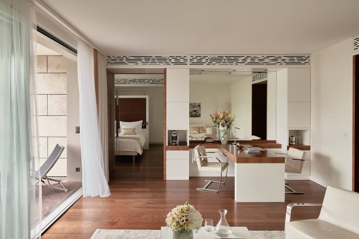 A modern hotel room with a balcony, a dining area, a kitchen, and a bedroom.
