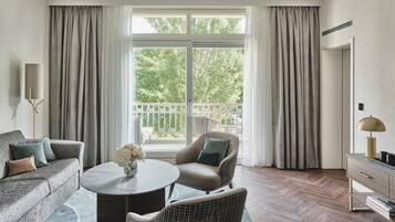 A modern living room with a sofa, armchair, and coffee table, a large window with curtains, and a view of the outdoors.