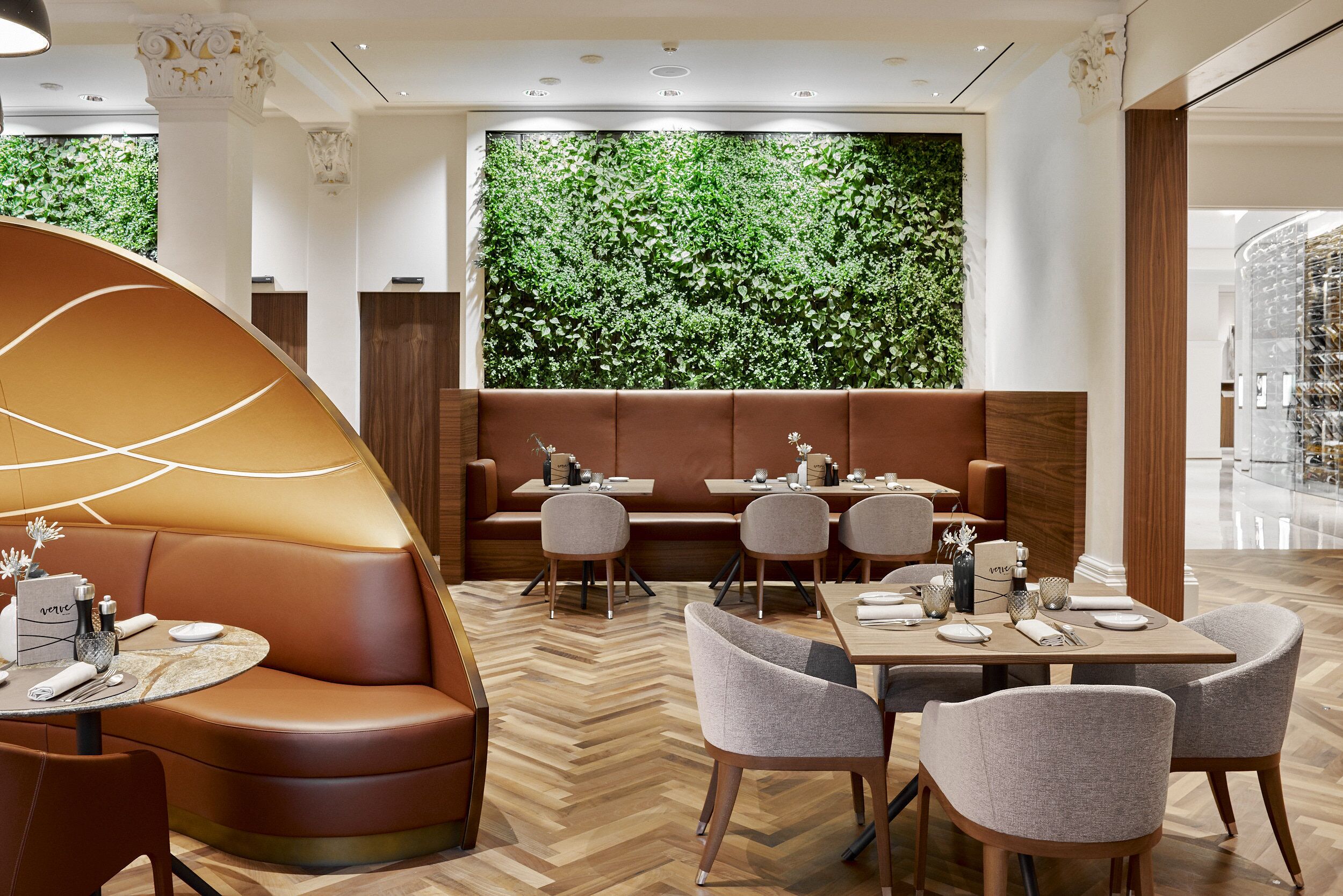 Ein modernes Restaurant mit Fischgratparkett, Ledersitzgelegenheiten und einer großen, begrünten Wand.