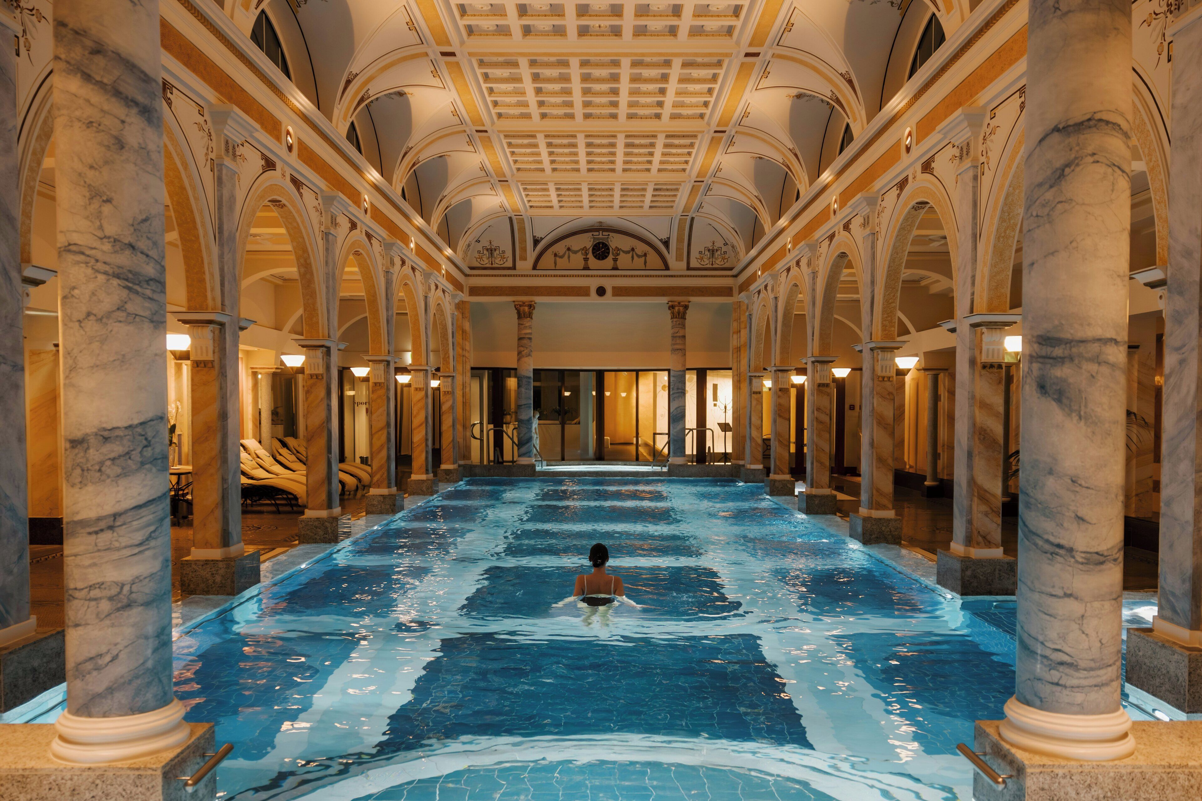 A large indoor swimming pool with marble columns and a high ceiling.