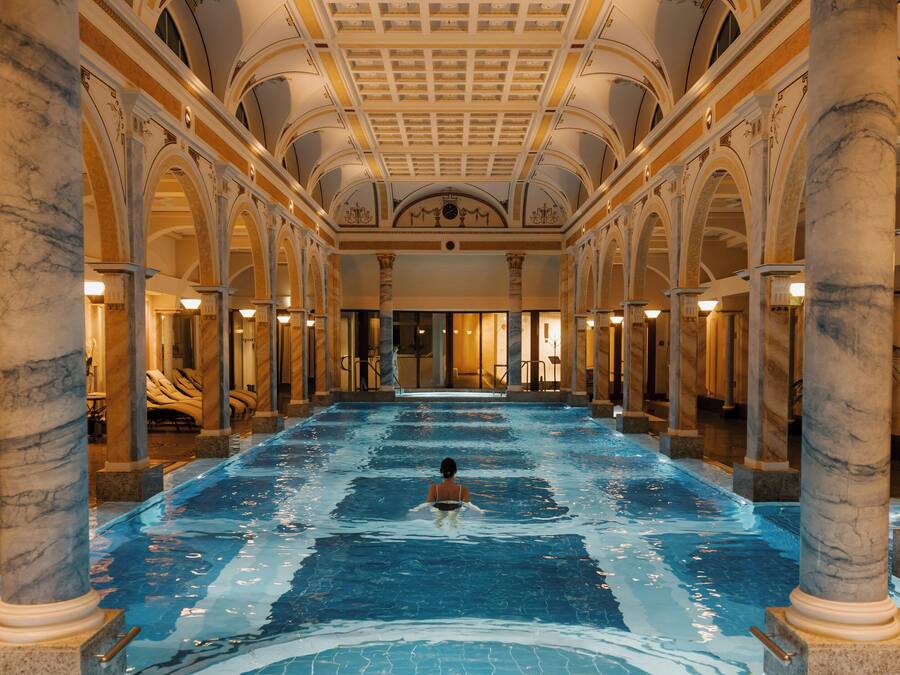 A large indoor swimming pool with marble columns and a high ceiling.