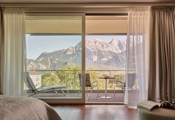 Une chambre avec un lit, un balcon doté d’une table et de chaises, et une vue sur la montagne.