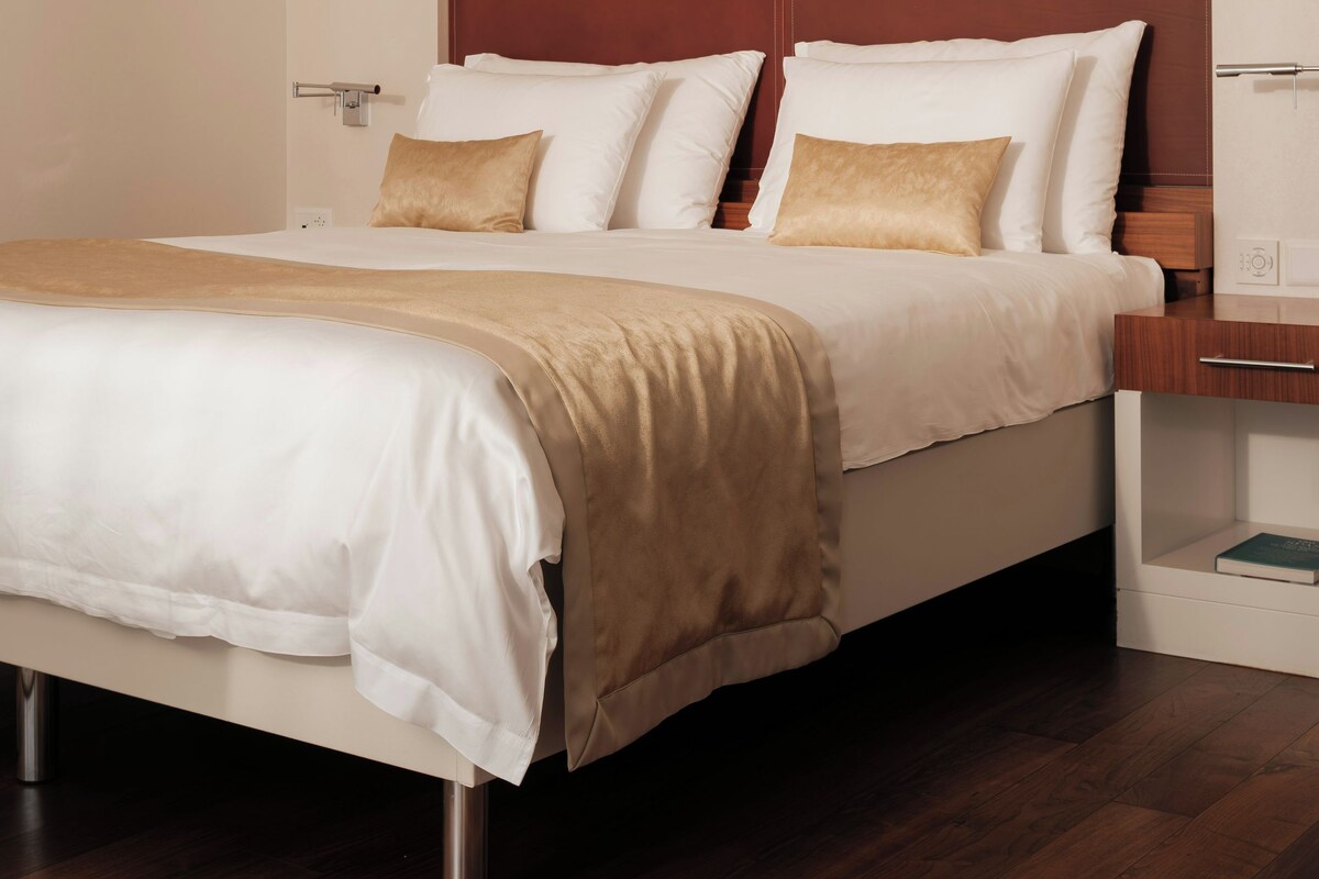 Una habitación de hotel moderna con una cama grande, cabecera de madera y una mesita de noche con un libro.