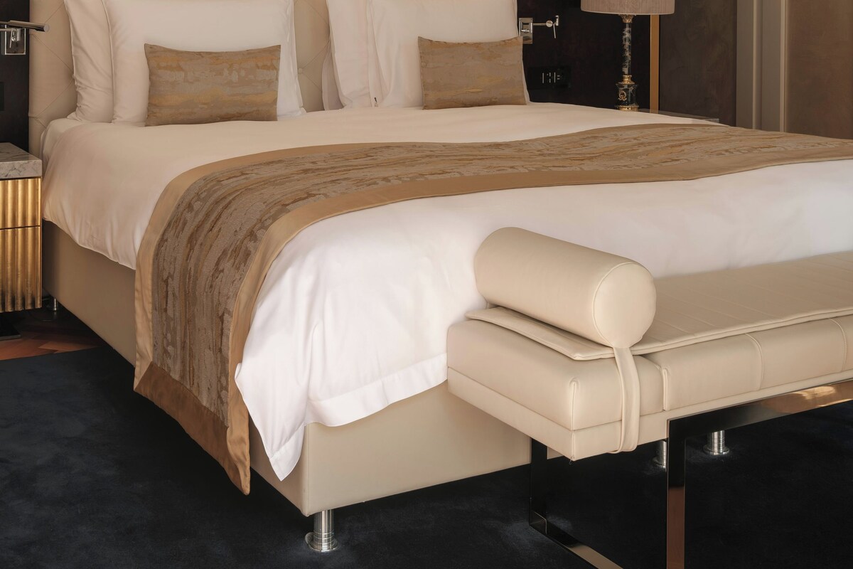 Una habitación de hotel moderna con una cama grande, una mesita de noche, una lámpara y una alfombra estampada.
