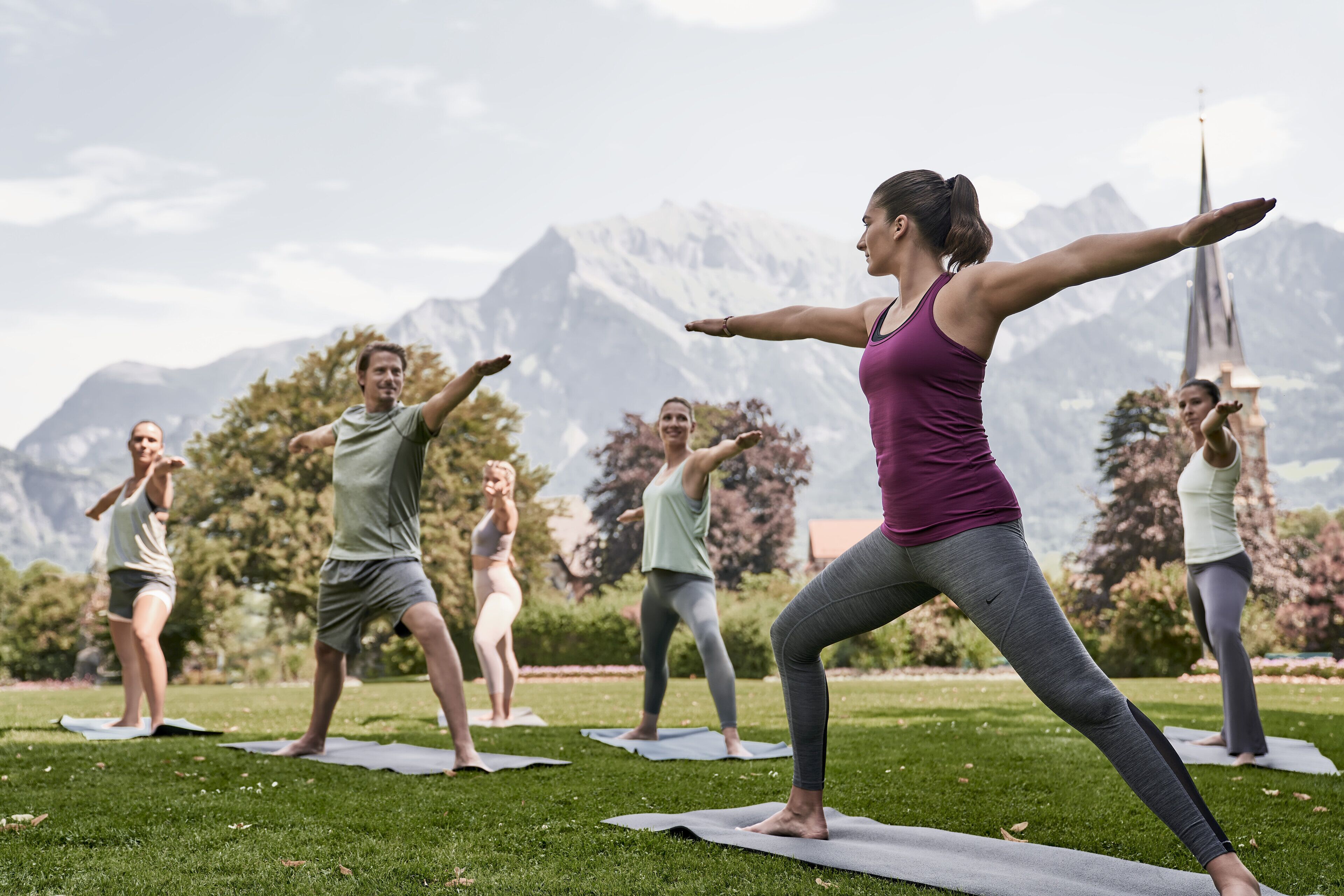 Un grupo de personas practicando yoga sobre esterillas en un entorno al aire libre, con montañas al fondo.