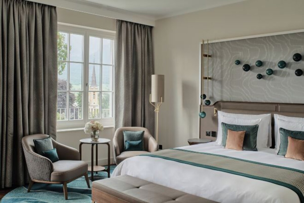 Una habitación de hotel con una cama grande, dos sillones, una mesita redonda y una lámpara.