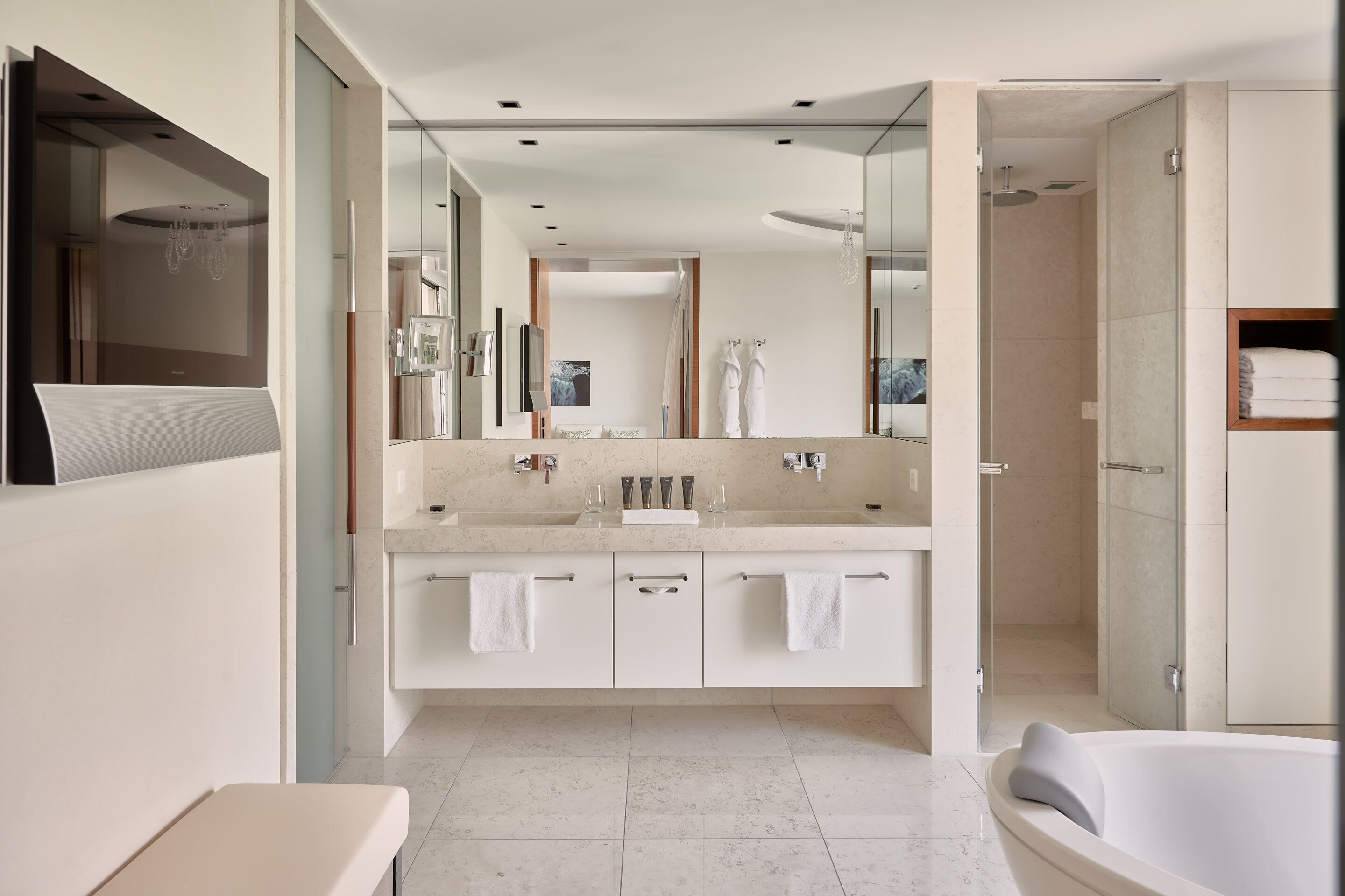 Un baño moderno con un espejo grande, lavamanos dobles, bañera y ducha a ras de suelo.