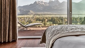 A bedroom with a large bed, a balcony with a chair, and a view of mountains.