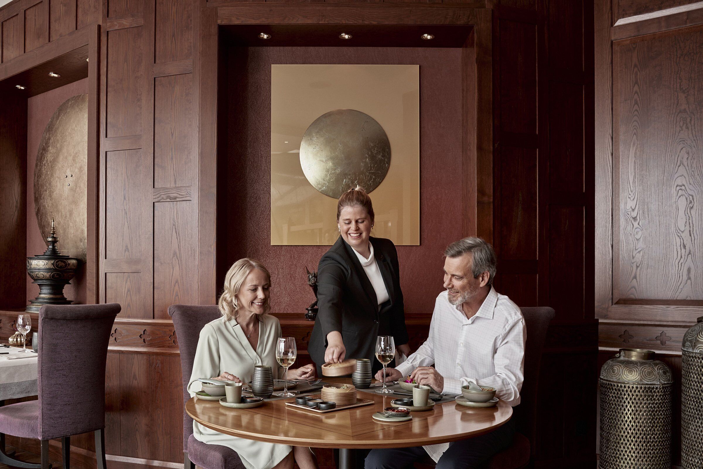 A dining area with a round table, chairs, and a waiter serving food.