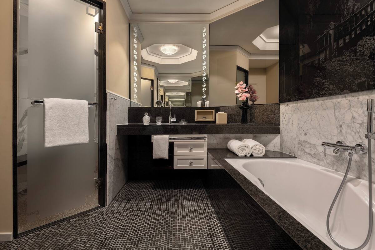 A modern bathroom with a glass shower door, a large mirror, a marble countertop, and a white bathtub.