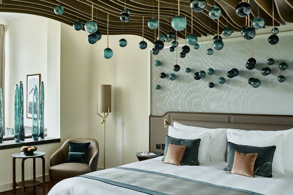 A hotel room with a large bed, a chair, a small table, and a wall with hanging spherical decorations.