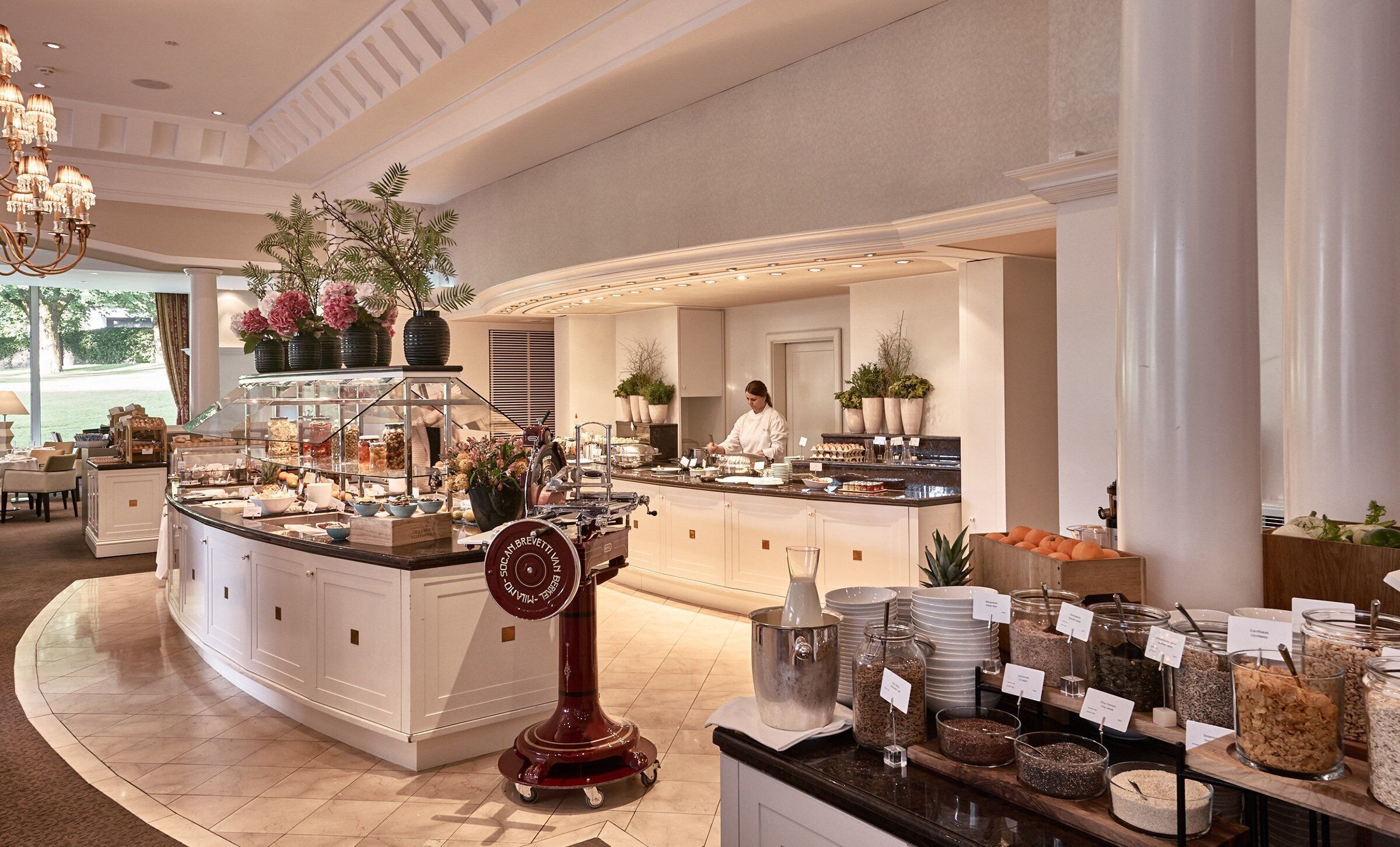 Um buffet de café da manhã com diversas opções de comida, um chef preparando alimentos e uma fonte decorativa.