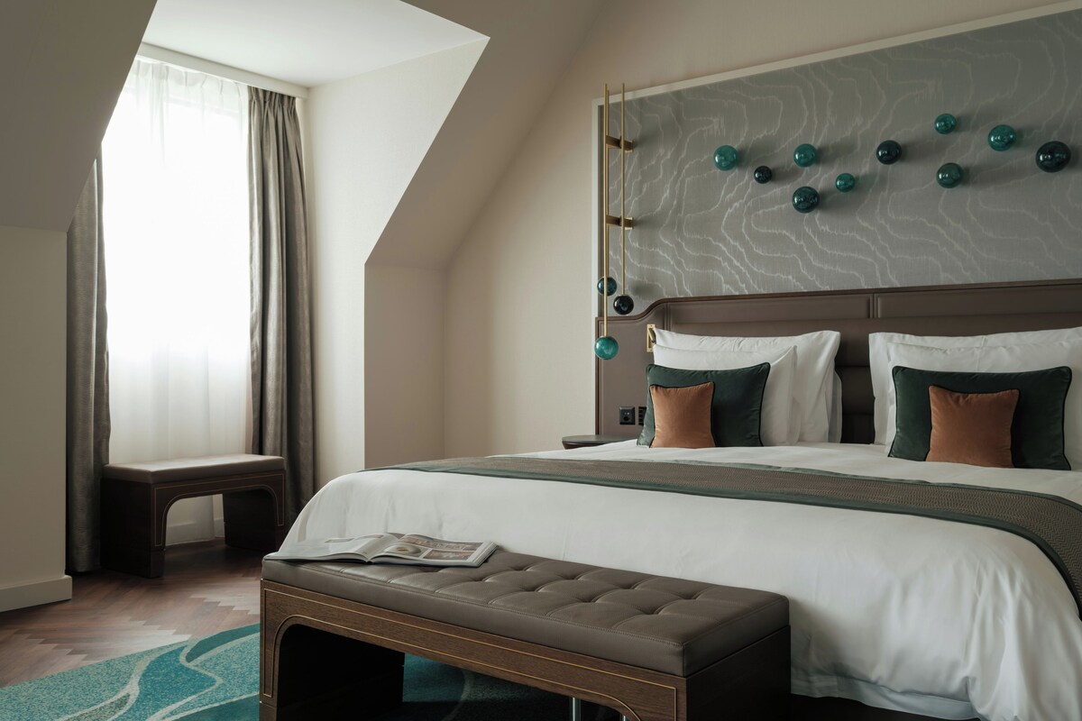 Habitación de hotel moderna con una cama grande, un banco y vistas al exterior.